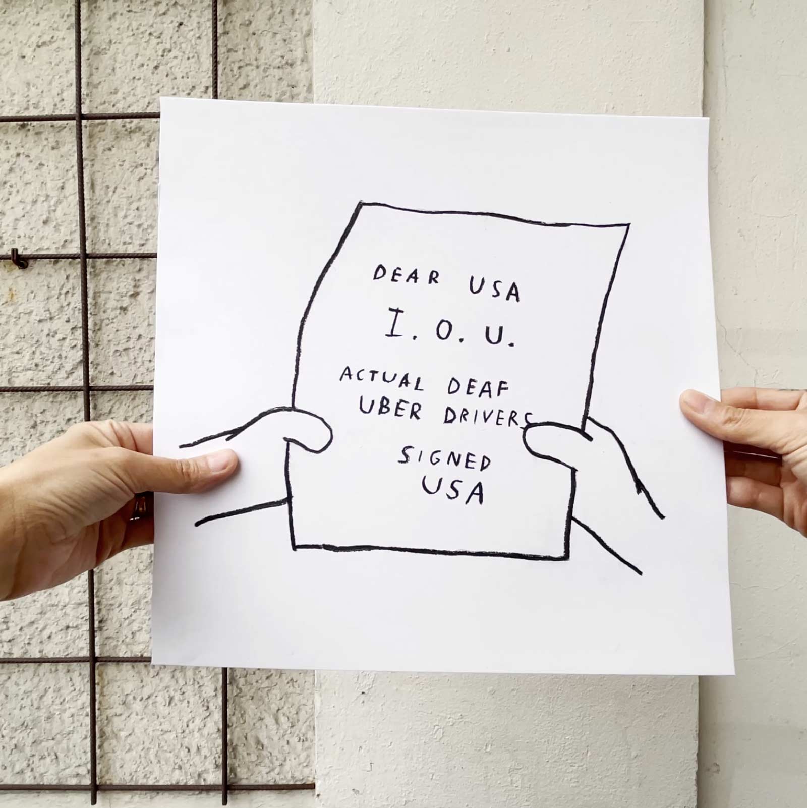 This still from IOU 4 USA depicts a square charcoal drawing held up by two hands. The drawing is of a frame from The Simpsons and shows an IOU note in Homer’s hands. The note reads: “DEAR USA I.O.U. ACTUAL DEAF UBER DRIVERS. SIGNED USA”.