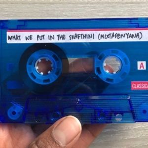 The artists hand appears holding a blue, slightly transparent audio cassette tape. On the top of the tape on a white label, the work title, “WHAT WE PUT IN THE SKAFTHINI (MIXAPENAYANA)” appears written in all-caps in black marker.